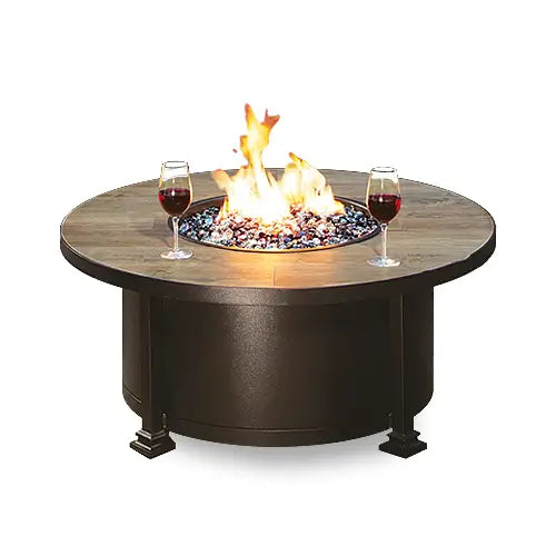 Round outdoor fire pit table with a brown base and stone top, featuring a recessed fire glass area. Ideal for patios and outdoor spaces