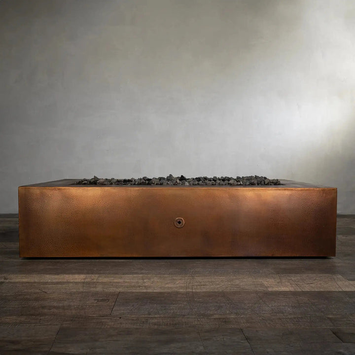 Front view of the Gravity Moreno 72x38 copper fire pit by Starfire Designs, showcasing the sleek, minimalist design with dark lava rocks inside