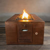 Close-up view of the Gravity Moreno 72x38 copper fire pit by Starfire Designs, featuring the propane tank access door with a warm, inviting flame in the background