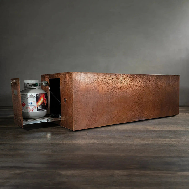 Side view of the Gravity Moreno 72x38 copper fire pit by Starfire Designs, featuring the extended hidden propane tank drawer with a hammered copper finish