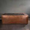 Side view of the Gravity Moreno 72x38 copper fire pit by Starfire Designs, showcasing its elegant hammered copper finish and spacious fire bed filled with black lava rocks