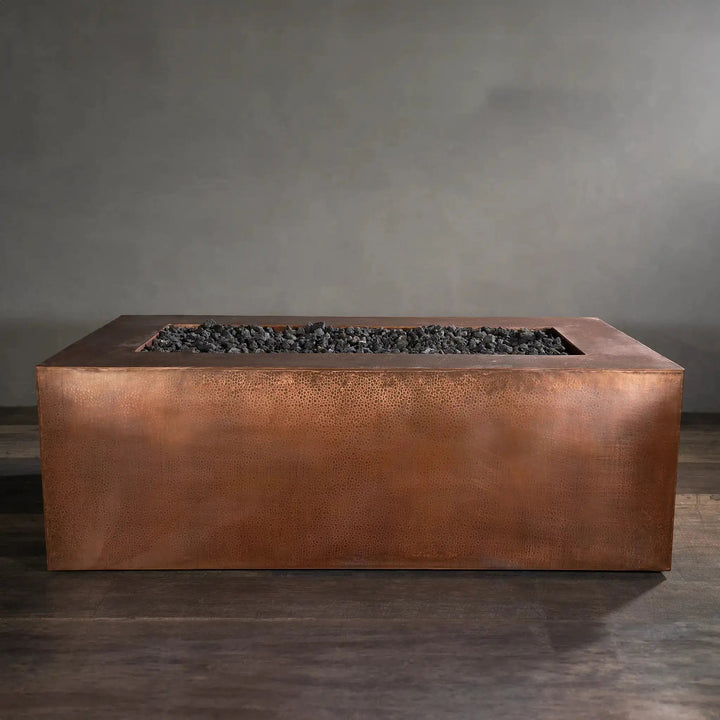 Side view of the Gravity Moreno 72x38 copper fire pit by Starfire Designs, showcasing its elegant hammered copper finish and spacious fire bed filled with black lava rocks