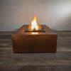 Side view of the Gravity Moreno 72x38 copper fire pit by Starfire Designs, featuring a single flame rising above dark lava rocks in a modern outdoor setting