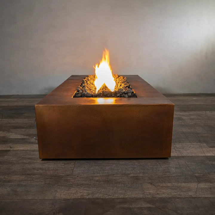 Side view of the Gravity Moreno 72x38 copper fire pit by Starfire Designs, featuring a single flame rising above dark lava rocks in a modern outdoor setting