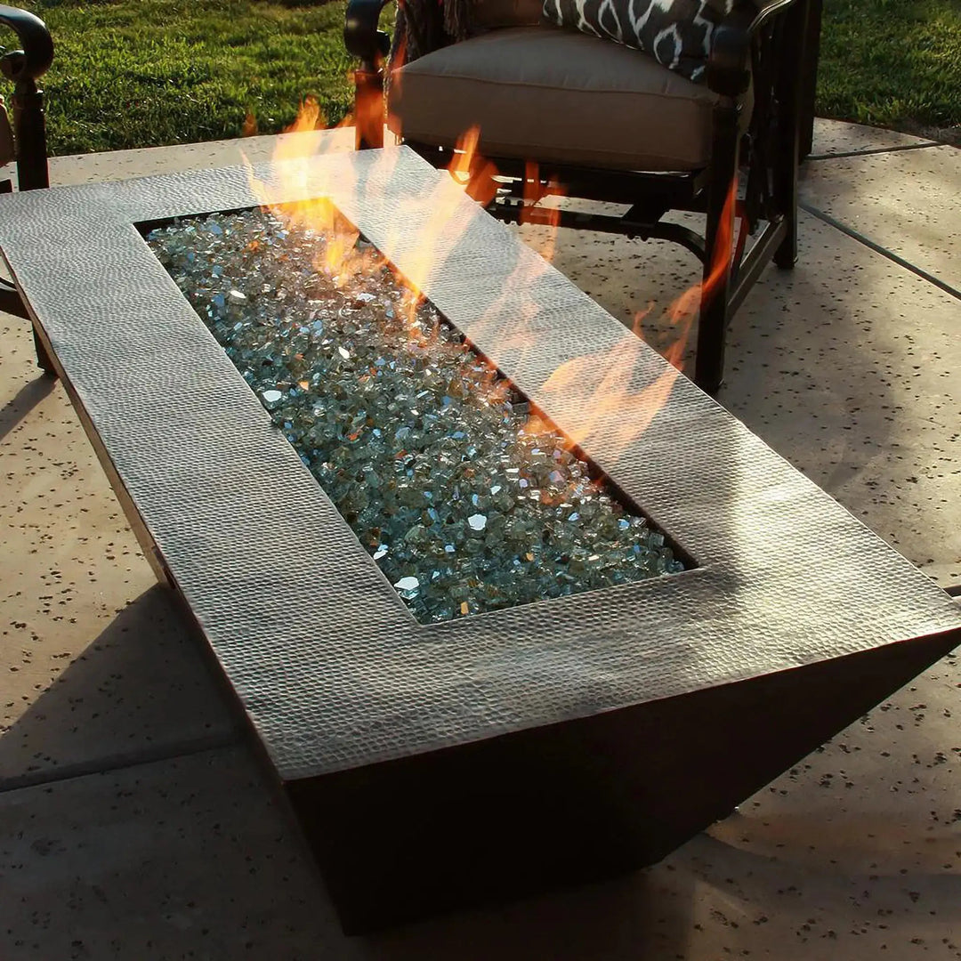 Closeup of Largo Moreno 60-inch x 26-inch Rectangle Copper Fire Pit, featuring a vibrant flame and reflective fire glass on a hand-hammered copper finish