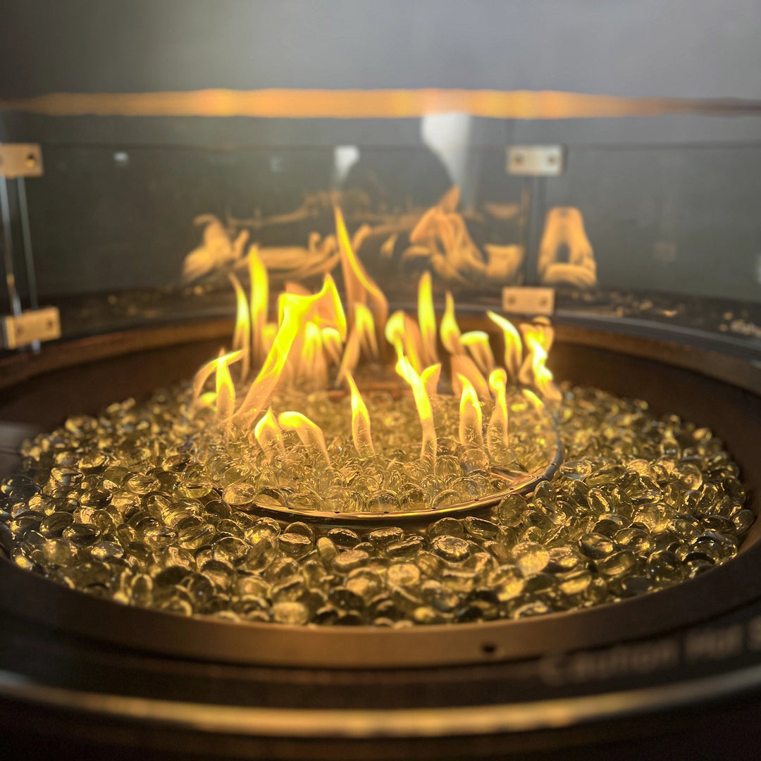 Close-up of the Golden Flame Malibu 44” Round Cast Aluminum Natural Gas Fire Table with golden flames reflecting off clear glass fire beads. Features a sleek circular design, highlighting the vibrant fire display.