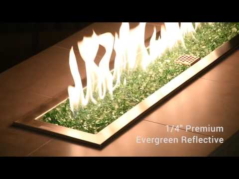 A modern linear fire feature showcases the rich, vibrant glow of 1/4" Evergreen Reflective Fire Glass by American Fire Products, with lush green tones and mirrored facets dancing beneath golden flames—perfect for adding fresh, organic elegance to any outdoor living space.