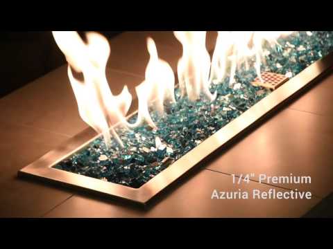 Mesmerizing flames dance across a bed of 1/4” Azuria Reflective Fire Glass by American Fire Products, showcasing its brilliant teal-blue tones and mirror-like sparkle in a modern outdoor fire feature.