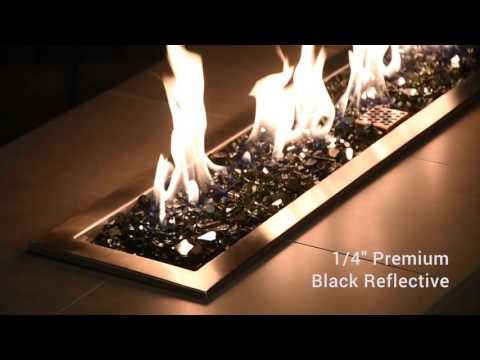 Dancing flames rise above a sleek bed of American Fire Products 1/4" black reflective fire glass, showcasing the striking contrast between glowing firelight and the polished, mirror-like surface of deep black glass—perfect for upscale, contemporary outdoor fire features.