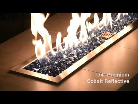 Vibrant cobalt blue 1/4" reflective fire glass from American Fire Products glowing beneath a lively flame in a contemporary outdoor fire feature, offering a bold pop of color and sparkling reflective shimmer perfect for modern patios or fire pit upgrades.
