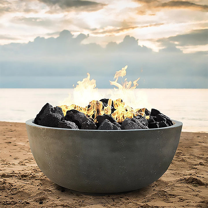 Prism Hardscapes Moderno 1 Gas Fire Bowl set on a sandy beach, featuring a large flame and natural gas setup with lava rock. This outdoor fire pit creates a stunning visual effect with the background of the ocean, ideal for luxurious beachside gatherings. Enhance your outdoor living space with a modern and large backyard fire pit, perfect for both commercial and residential use.