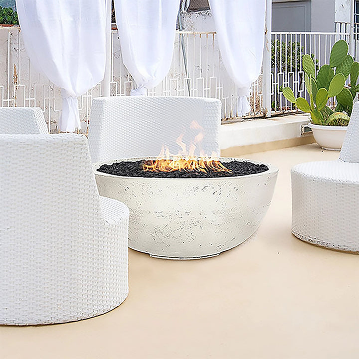 Prism Hardscapes Moderno 1 Gas Fire Bowl showcased in a chic outdoor lounge with white furniture. The fire pit provides a stylish contrast with its natural concrete finish and black lava rock, making it the focal point for a modern patio or outdoor space. A perfect solution for those looking to add warmth and sophistication to their backyard or commercial settings