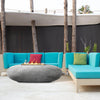 Prism Hardscapes Pebble Gas Fire Pit placed on a stylish black and white geometric patterned outdoor rug, with wicker patio furniture surrounding it. This round gas fire pit's elegant design offers a natural concrete finish, perfect for cozy backyard settings. Its large, smooth surface provides a focal point for outdoor entertaining. Modern fire pit, outdoor patio fire pit, fire pit natural gas, large backyard fire pit, concrete fire bowl
