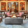 A luxury deck features the Prism Hardscapes Tavola 3 Gas Fire Pit as its centerpiece, surrounded by modern outdoor furniture. This contemporary fire pit is made of high-quality concrete and is powered by propane, providing a clean and efficient flame. The design is both sleek and functional, perfect for creating a warm atmosphere on cool evenings. The fire pit's neutral tone blends seamlessly with the deck and surrounding landscape, offering a refined addition to any outdoor living space.