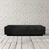 Prism Hardscapes Tavola 5 gas fire pit in ebony, featured in a sleek studio setup with a modern white brick wall. The rectangular fire pit showcases a dark, smooth black finish, designed for contemporary outdoor spaces, with a recessed burner containing black lava rocks. 