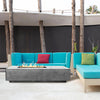A vibrant outdoor lounge setup featuring colorful cushions and the sleek, rectangular Prism Hardscapes Tavola 5 Gas Fire Pit in the center. This fire pit serves as the focal point of the seating area, offering both warmth and a contemporary aesthetic. Its smooth concrete finish complements the lively, modern design of the space. 