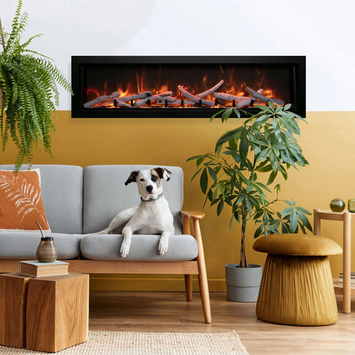 A cozy living room featuring the Remii Tall Indoor/Outdoor Built-In Electric Fireplace with vibrant orange flames and realistic log media. The sleek black frame complements modern interiors, creating a welcoming ambiance, while a dog lounges nearby.