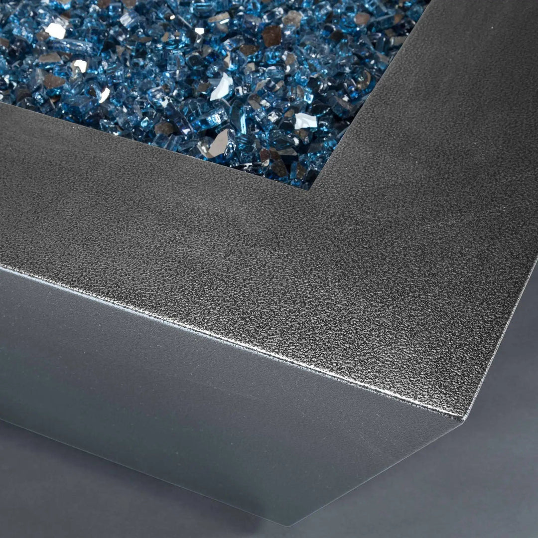  Close-up of the Starfire Designs Steel Mill 48-inch by 32-inch Rectangle Gas Fire Pit in Silver Hammertone finish, featuring a textured corner and filled with sparkling blue fire glass