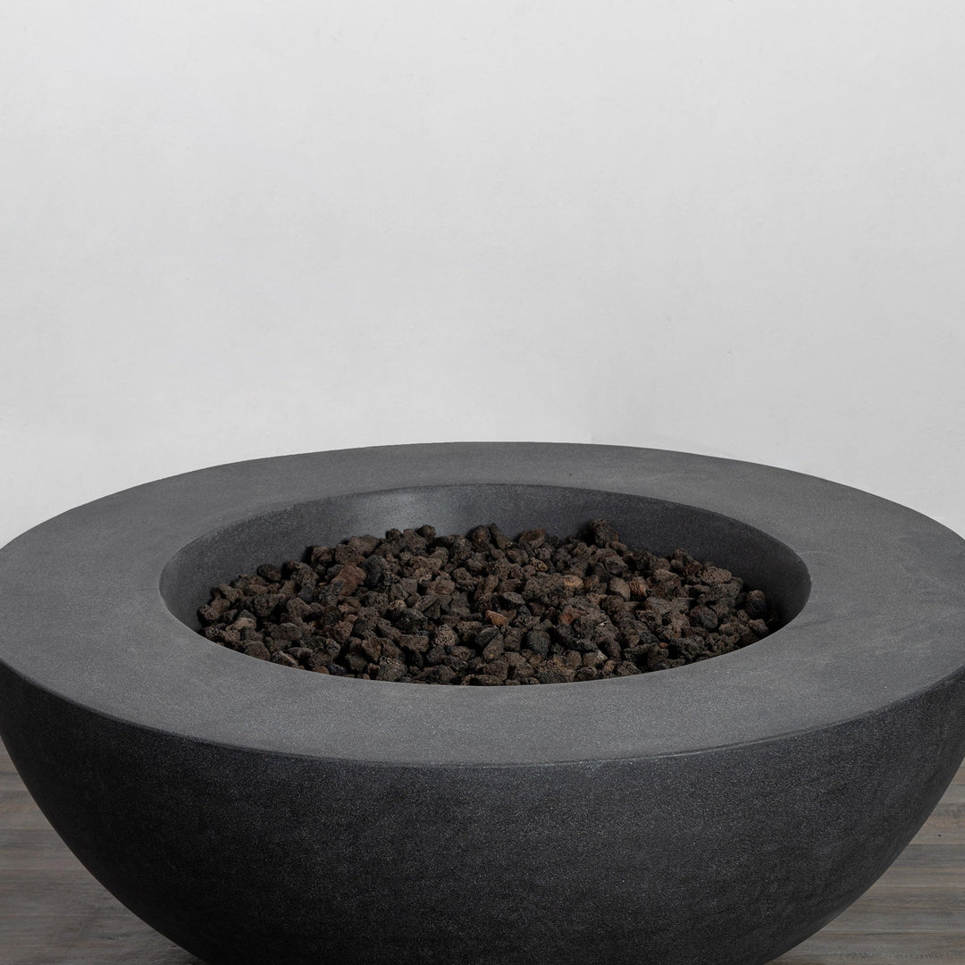 The Starfire Designs Beton 42 Inch Graphite Round Concrete Natural Gas Fire Pit filled with high-quality black lava rocks, creating a natural and modern outdoor ambiance with its sturdy concrete construction and sophisticated graphite finish.