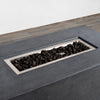 Close-up of the burner area filled with premium black lava rocks in the Starfire Designs Beton 55" Graphite Rectangle Hidden Propane Tank Gas Fire Pit. The natural stones enhance heat distribution while complementing the graphite concrete body. Keywords: lava rock fire pit, backyard ambiance, propane fire feature.