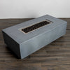 Angled view of the Starfire Designs Beton 55-inch natural gray rectangle gas fire pit filled with decorative lava rocks, designed to retain heat and enhance the fire pit’s visual allure. The natural gray concrete contrasts beautifully against the earthy tones of the media.