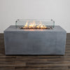 Full front view of the Starfire Designs Beton 55" Natural Gray Rectangle Hidden Propane Tank Gas Fire Pit with flames glowing inside the tempered glass wind guard. The glass enclosure enhances safety and adds elegance to the modern fire pit design, perfect for outdoor entertaining.