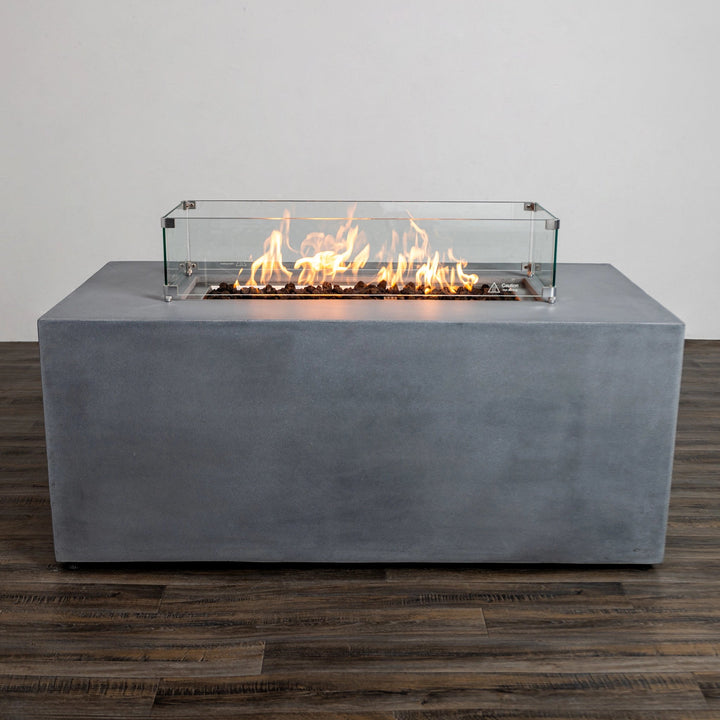 Full front view of the Starfire Designs Beton 55" Natural Gray Rectangle Hidden Propane Tank Gas Fire Pit with flames glowing inside the tempered glass wind guard. The glass enclosure enhances safety and adds elegance to the modern fire pit design, perfect for outdoor entertaining.