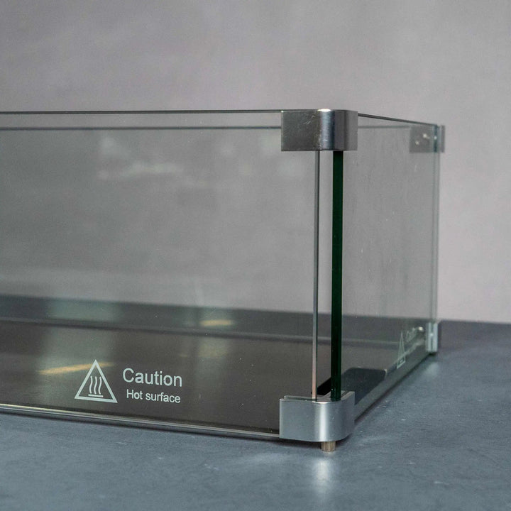 Close-up view of the Starfire Designs Beton Rectangle Glass Wind Guard, highlighting the sturdy corner construction and caution label for hot surfaces