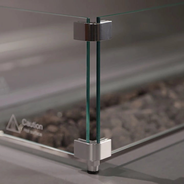 Close-up of Starfire Designs Beton Square Glass Wind Guard corner detailing. Durable tempered glass panels held by silver brackets ensure stability and safety. Ideal for windy environments, this accessory enhances the functionality and design of modern fire pits and tables.