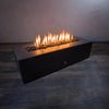 A lifestyle image showcasing the Starfire Designs Fire Pebbles set in black, arranged in a modern rectangular fire pit with the flames fully lit. The smooth black pebbles add a contemporary and sleek look to the fire feature. Perfect for creating an elegant, modern ambiance in outdoor spaces.