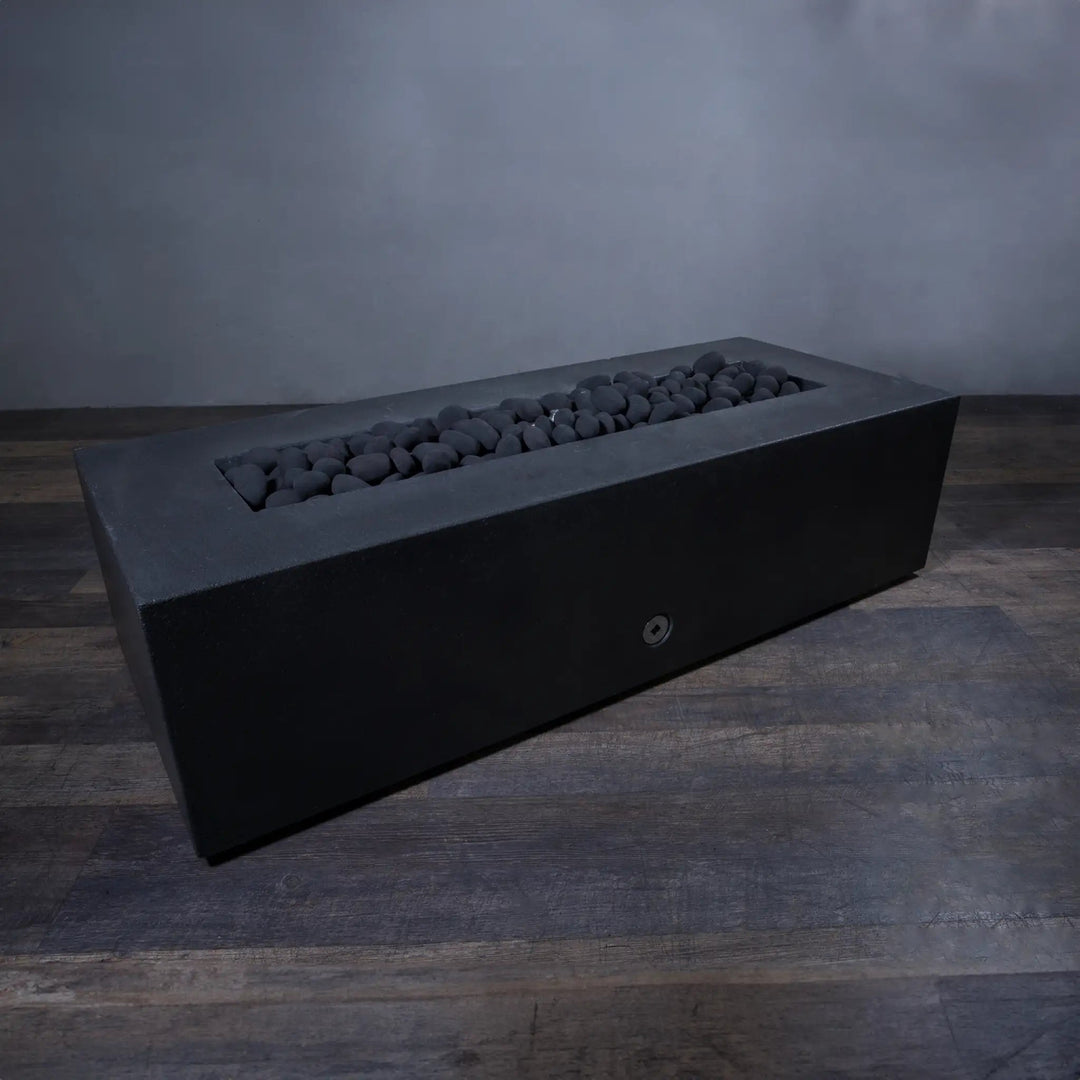 A lifestyle image featuring the Starfire Designs Fire Pebbles in black, displayed in an unlit rectangular fire pit. The arrangement of smooth, dark pebbles contrasts against the fire pit's sleek design, creating a refined, minimalist appearance. Ideal for enhancing modern outdoor settings with style.
