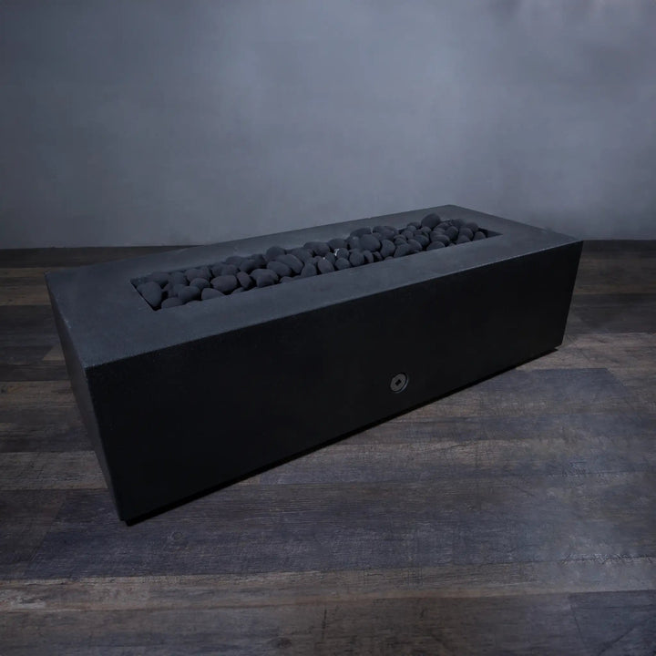 A lifestyle image featuring the Starfire Designs Fire Pebbles in black, displayed in an unlit rectangular fire pit. The arrangement of smooth, dark pebbles contrasts against the fire pit's sleek design, creating a refined, minimalist appearance. Ideal for enhancing modern outdoor settings with style.