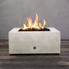 A front view of the Starfire Designs Gravity 36" Square Concrete Gas Fire Pit in white, featuring a robust flame rising from the fire pit’s lava rock fill. The sleek, modern concrete design complements outdoor spaces and is perfect for both residential and commercial use