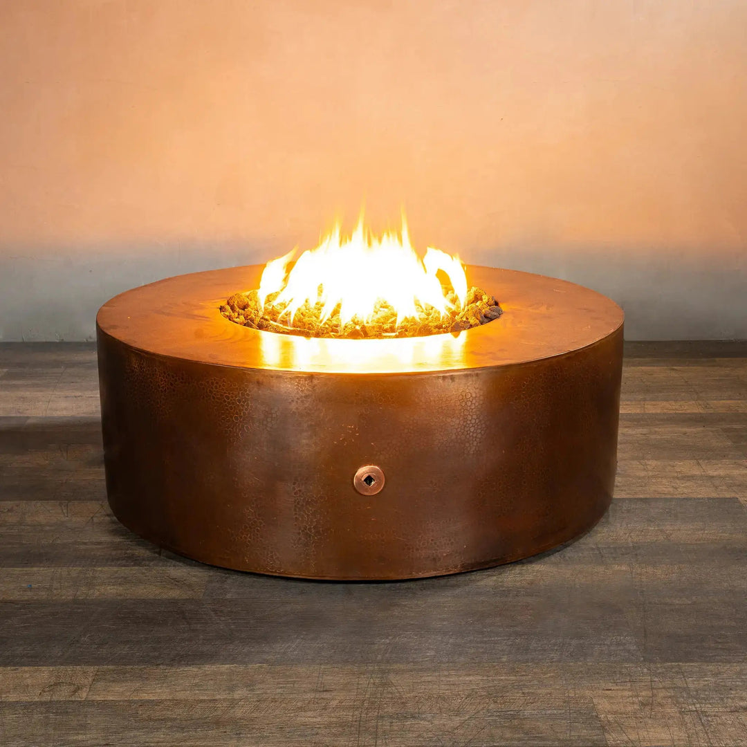 Gravity Moreno 45-inch round copper fire pit by Starfire Designs with a vibrant fire glowing brightly, highlighting the hammered copper finish and the inviting warmth it offers in a modern indoor setting.