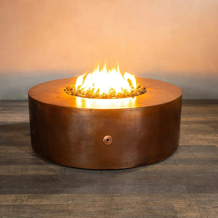 Gravity Moreno 45-inch round copper fire pit by Starfire Designs with a vibrant fire glowing brightly, highlighting the hammered copper finish and the inviting warmth it offers in a modern indoor setting.