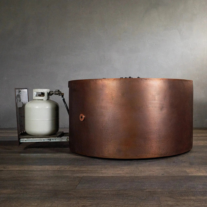 Side view of the Gravity Moreno 45-inch round copper fire pit by Starfire Designs with the propane tank drawer pulled out, showcasing the ease of access for refueling and the sturdy, handcrafted copper finish
