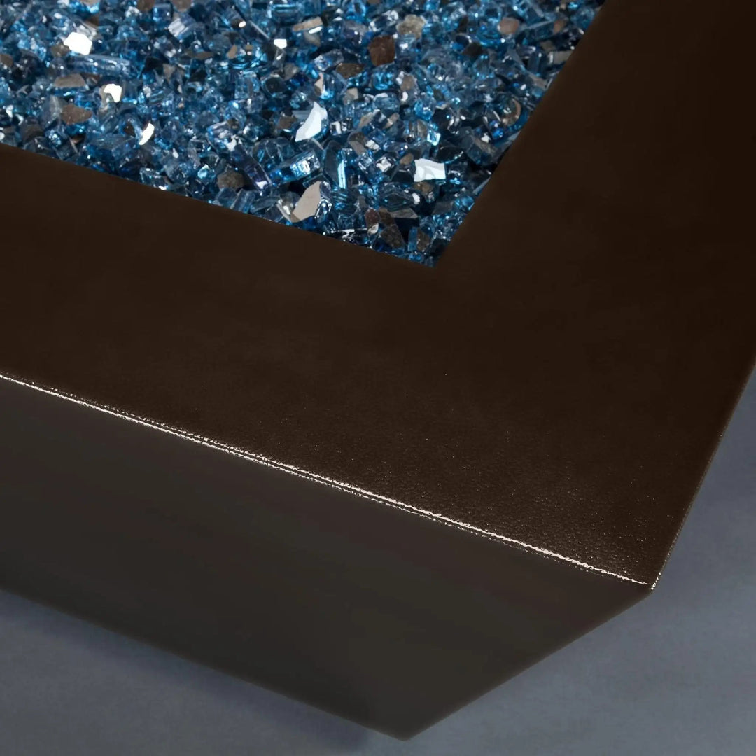 Close-up view of the corner of the Steel Mill 48-inch by 32-inch Rectangle Gas Fire Pit - Bronze Hammertone, featuring blue fire glass. Durable steel construction with a bronze hammertone finish