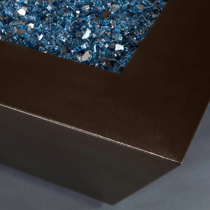 Close-up view of the corner of the Steel Mill 48-inch by 32-inch Rectangle Gas Fire Pit - Bronze Hammertone, featuring blue fire glass. Durable steel construction with a bronze hammertone finish