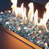 A vibrant close-up of Starfire Glass 1/2" Broken Fire Glass in Azuria color, glowing under flickering flames in a rectangular fire pit. The reflective finish enhances the shimmer, making it an ideal choice for modern fire pits. 