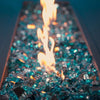 Close-up of Azuria Starfire 1/2" Broken Fire Glass, sparkling with reflective shine beneath a dancing fire. Perfect for enhancing gas fire pits with a contemporary touch.
