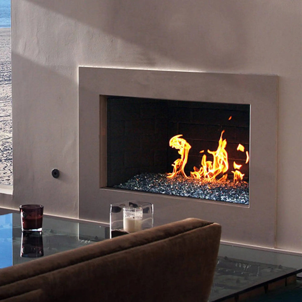A backyard fire pit with Starfire Glass 1/4" Broken Pre-Mixed Fire Glass (10lbs) in ocean blue and clear hues, reflecting the bright flames in a cozy outdoor patio setting. Surrounded by stone veneer, this gas fire pit enhances the ambiance, making it a stunning addition to any outdoor space. This fire glass is heat-resistant, durable, and ideal for outdoor gas fire pits, adding elegance and function to your backyard.