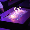 A stylish rectangular fire table illuminated with clear Starfire Glass Reflective Fire Diamonds, enhanced by purple LED accent lighting. The fire glass crystals sparkle under the flames, offering a contemporary fire pit design for upscale outdoor lounges and patios. Works perfectly with natural gas and propane fire pits.