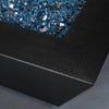 A close-up of the corner of the Starfire Designs Steel Mill 60" x 32" Rectangle Gas Fire Pit in a Silver Vein finish, highlighting the smooth, angular design and filled with sparkling blue fire glass. The fire pit’s sturdy construction and textured silver surface make it an elegant addition to any outdoor patio setting. Perfect for outdoor fire features, luxury fire pits, and glass media.