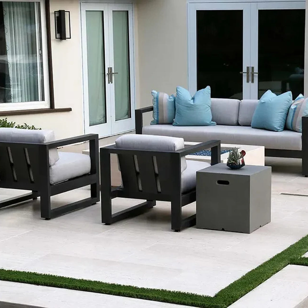 Modern patio furniture set with a sofa, two armchairs, a side table, and light cushions accented with blue pillows in an outdoor space