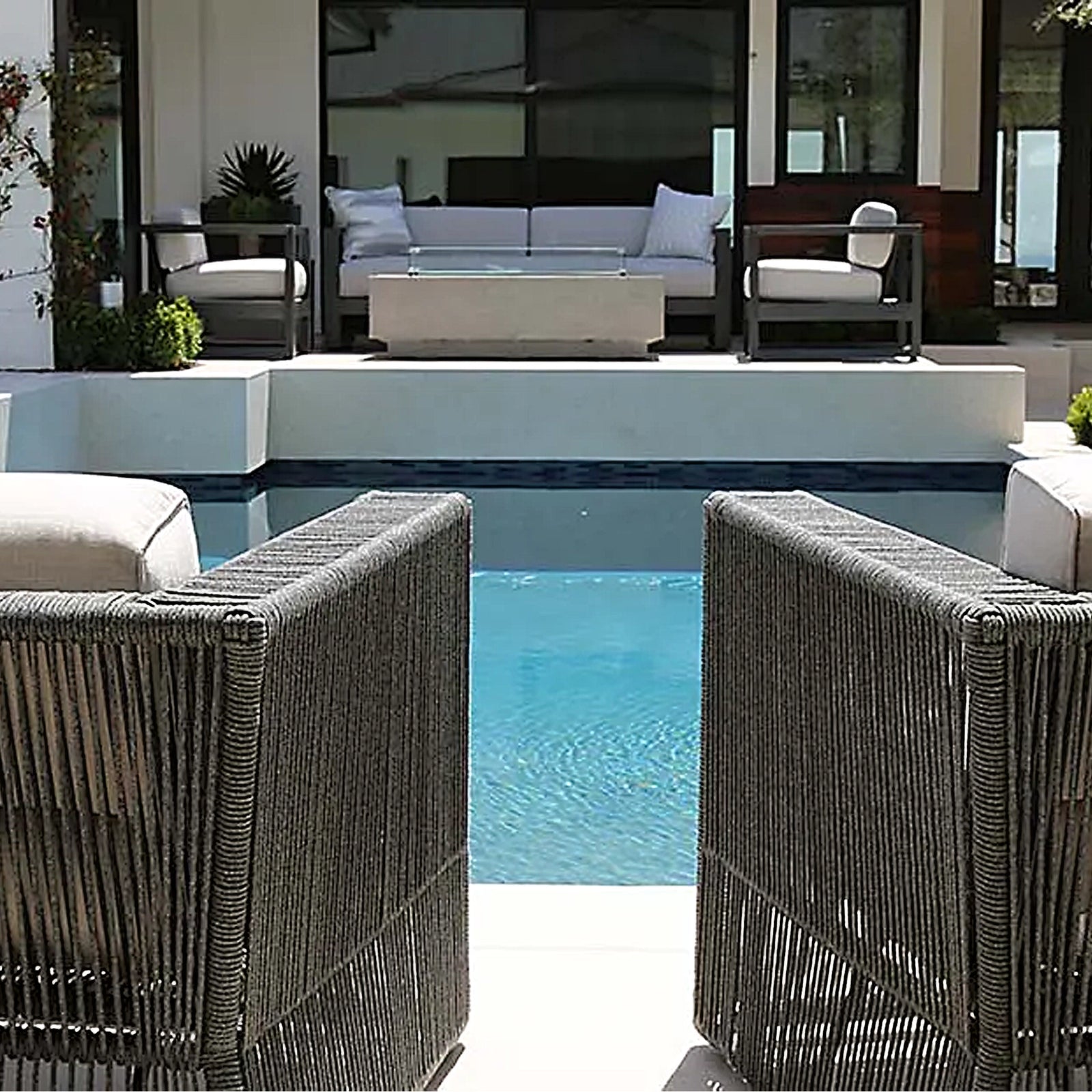 Luxury outdoor patio setting featuring a swimming pool, modern woven chairs, a sofa, and a fire table