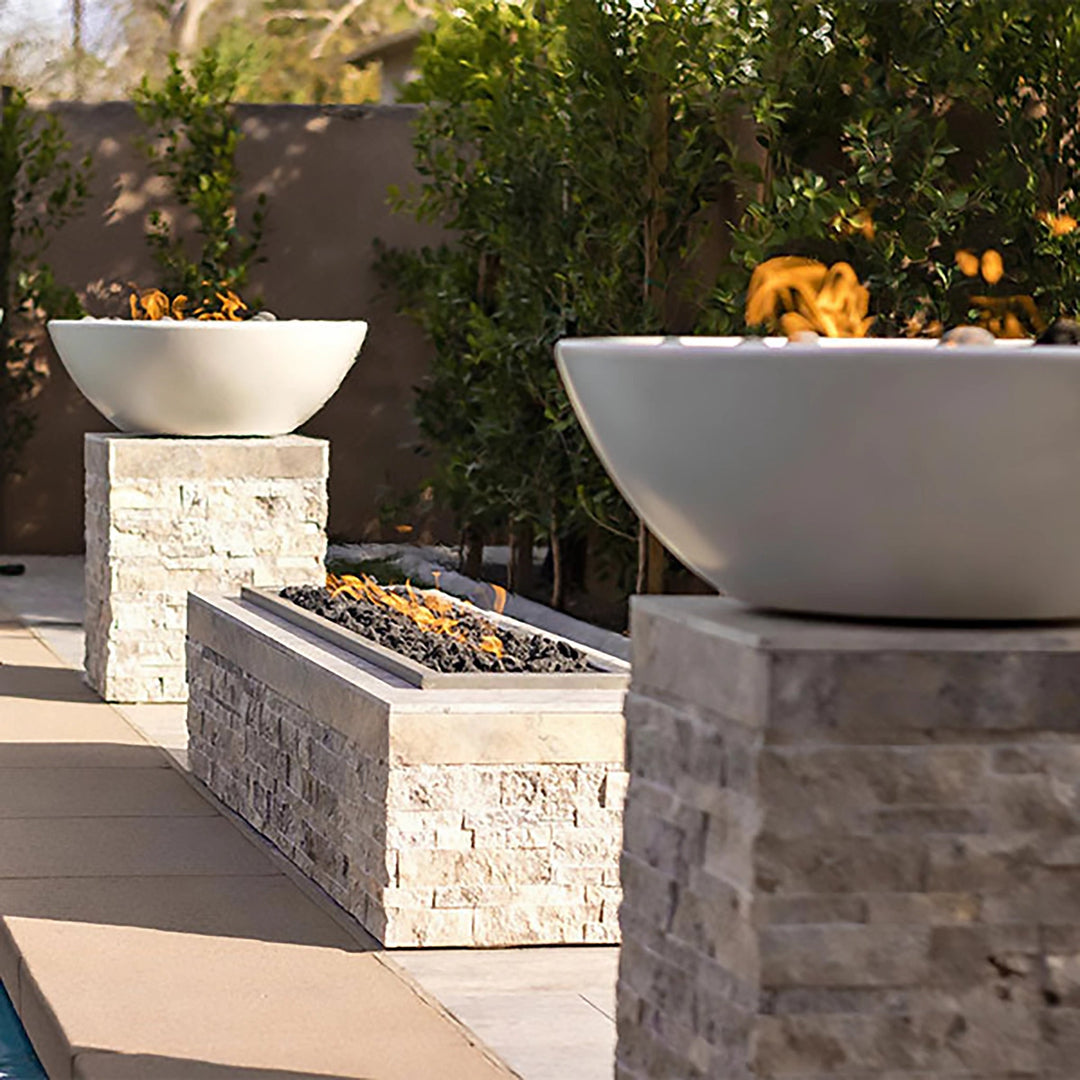 The Outdoor Plus 27-inch Round Concrete Sedona Fire Bowls displayed in a sophisticated garden setup, surrounded by stone pillars and lush greenery. The clean lines of the fire bowl blend with the natural landscape, creating a peaceful ambiance. Perfect for high-end outdoor designs, these fire bowls add warmth and style to garden spaces, making them ideal for enhancing the beauty of outdoor settings
