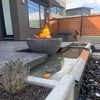 The Outdoor Plus 27-inch Round Concrete Sedona Fire Bowl installed in a contemporary backyard setting, placed next to a sleek water feature. The modern design of the fire bowl complements the surrounding architecture, blending fire and water elements for a serene and luxurious atmosphere. This installation is ideal for modern outdoor spaces, adding warmth and visual interest to sophisticated patios and gardens