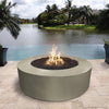 The Outdoor Plus 42-inch Occasional Height Florence Concrete Gas Fire Pit shown in a luxurious poolside setting. This modern, low-profile fire pit adds warmth and elegance to outdoor environments, featuring a smooth round design in a concrete finish. Perfect for use with natural gas or propane to enhance patio ambiance