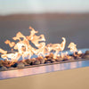 Close-up image of The Outdoor Plus 48" Coronado Steel Gas Fire Pit, showcasing vibrant flames dancing over natural lava rock. This modern gas fire pit features a sleek steel finish, ideal for contemporary outdoor settings. Its high-quality materials ensure durability and resistance to various outdoor elements, making it a perfect addition to any patio or backyard entertainment space. Ideal for creating a cozy atmosphere with its powerful and elegant flame display.