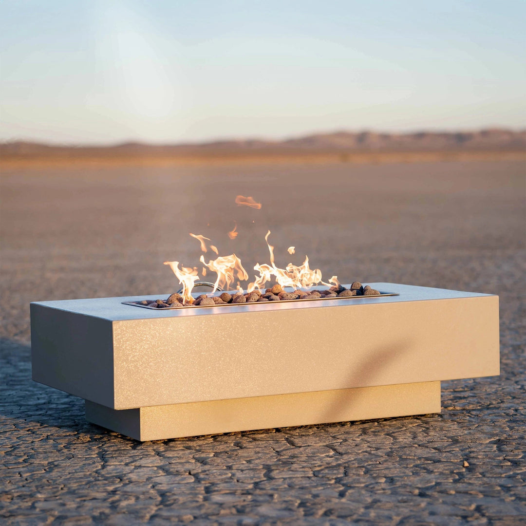 The Outdoor Plus 48" Coronado Steel Gas Fire Pit placed in a serene desert setting, highlighting its geometric design and substantial size. The fire pit's steel body contrasts beautifully against the natural landscape, and the flames create a captivating focal point. Perfect for outdoor gatherings, this modern fire pit offers both style and functionality with its durable construction and eye-catching flame presentation.